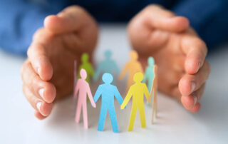 A man's hands holding a group of colored paper people, providing Proposal Support for the Federal Government.